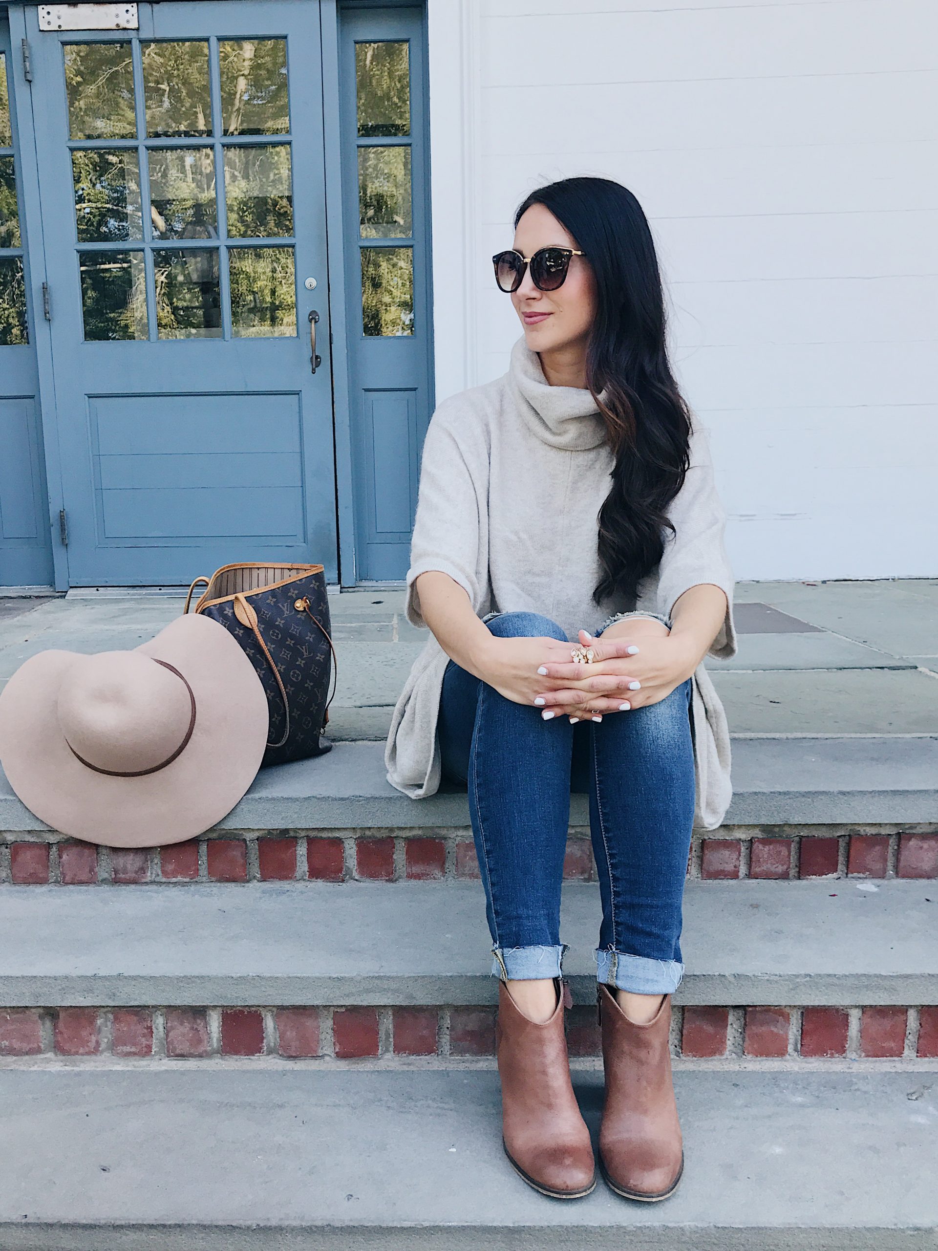 blogger Anna Monteiro of Blushing Rose Style blog wearing fall outfit poncho, brown ankle booties and oversized sunglasses.