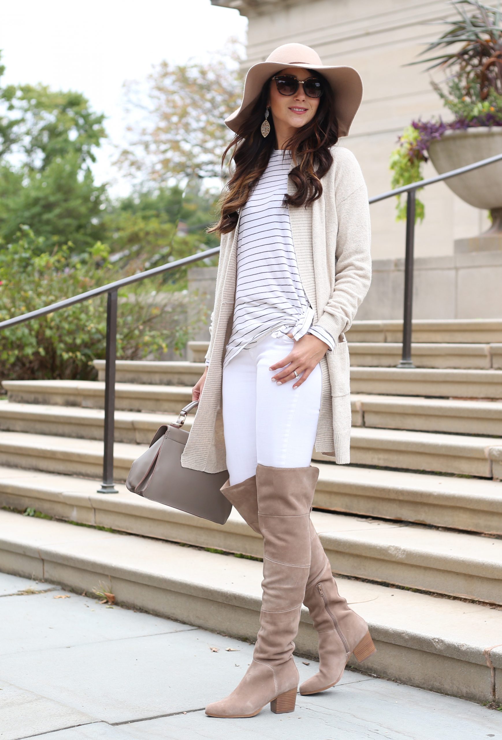 blogger Anna Monteiro of blushing rose style blog wearing cozy fall sweaters and cream color cardigan with striped tee and over the knee boots in this cute fall outfit with floppy hat