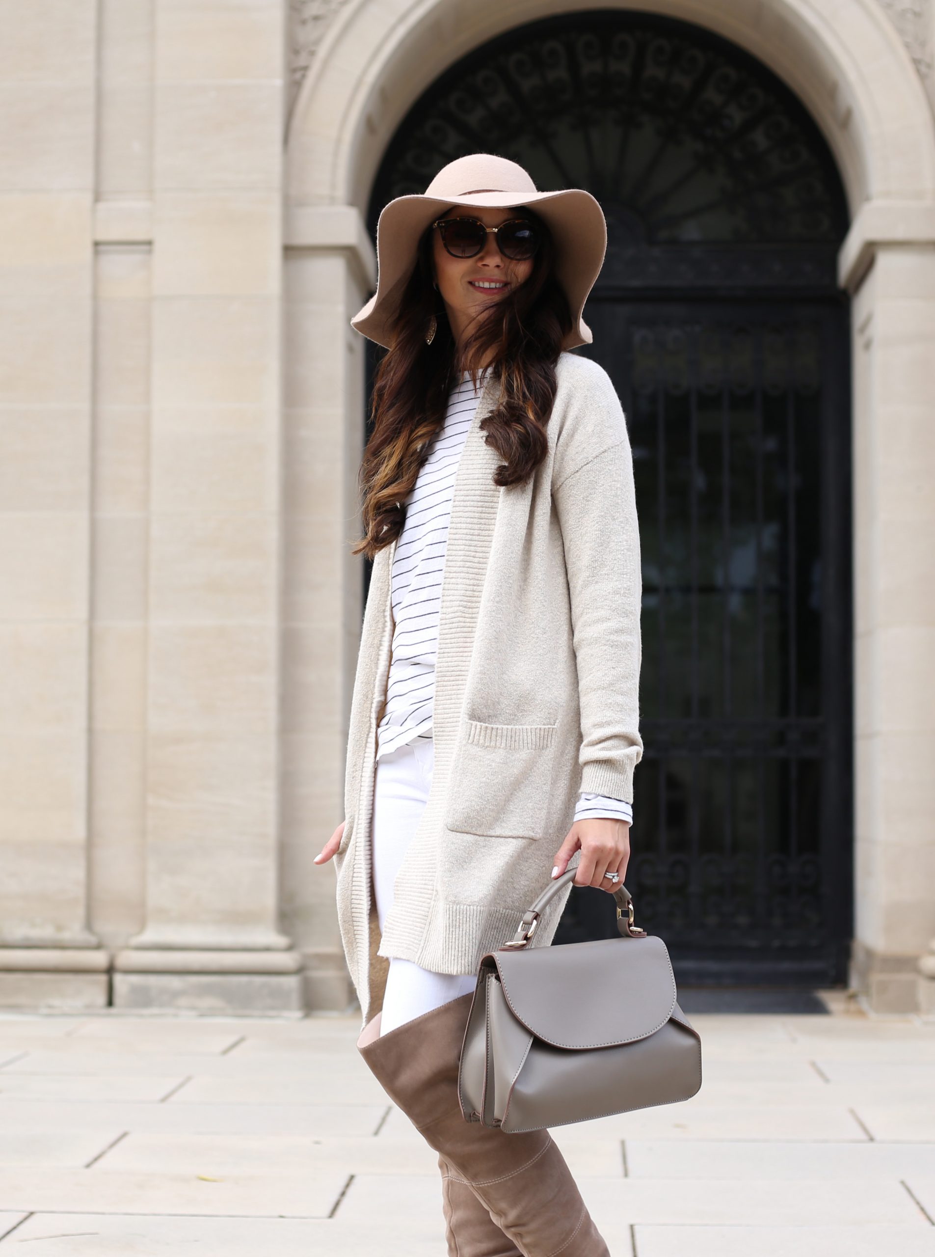 blogger Anna Monteiro of Blushing Rose Style wearing cozy fall sweater with white skinny jeans and taupe over the knee boots cream cardigan and floppy hat in this cute fall outfit