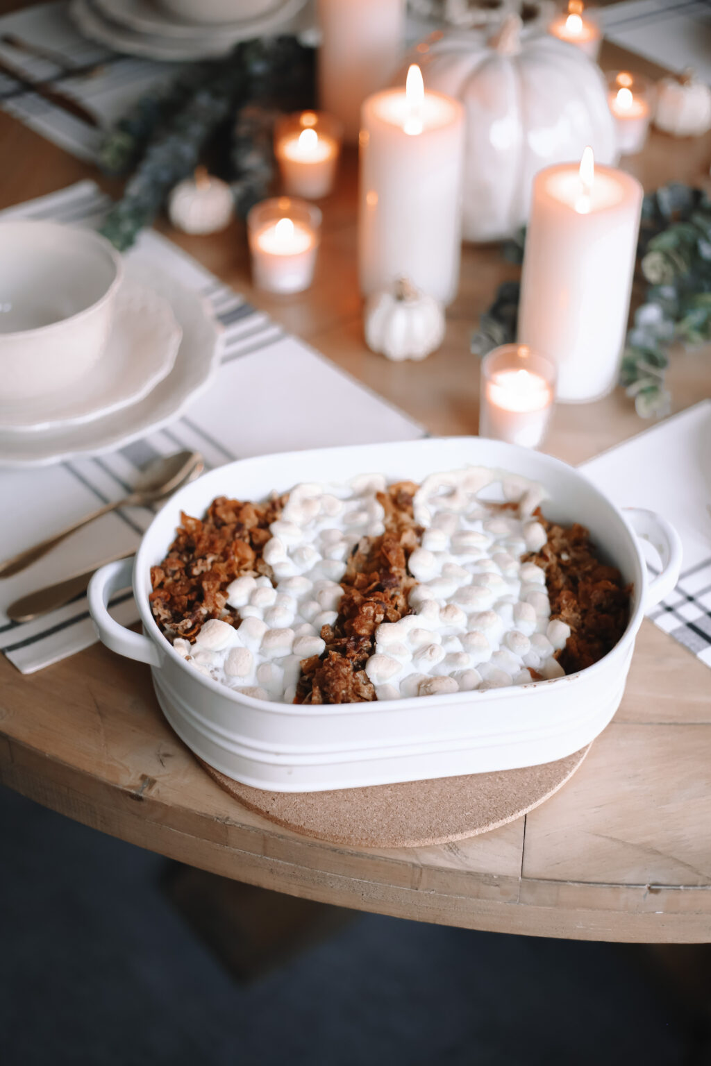 Homemade Thanksgiving sweet potato casserole topped with toasted marshmallows and pecan crumble in a white baking dish on a festive holiday table.
